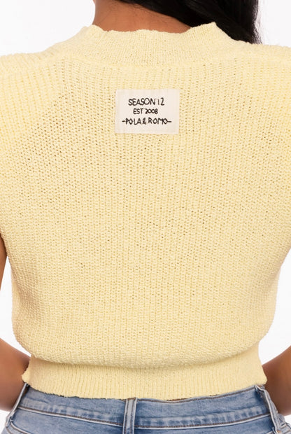 Close-up of a woman wearing a yellow knit top.